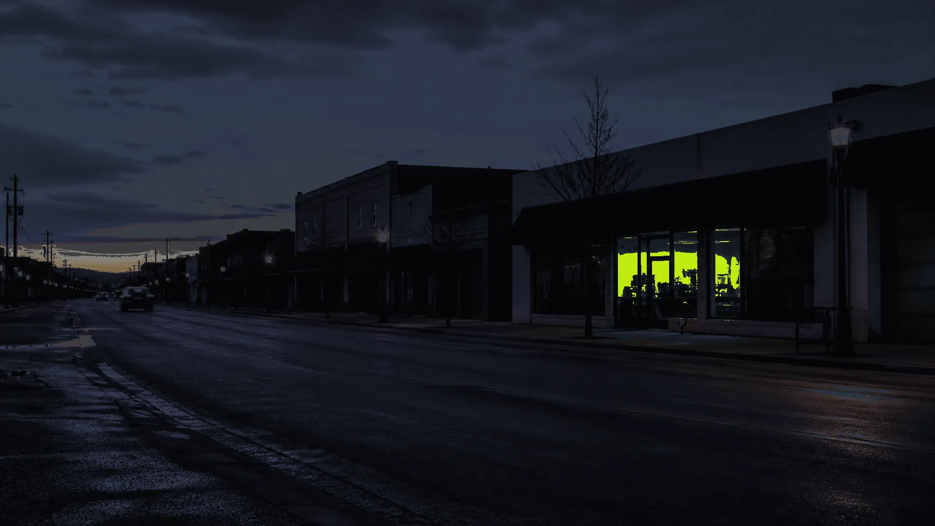 Dark service storefront at dusk with one bright workroom still active after hours.
